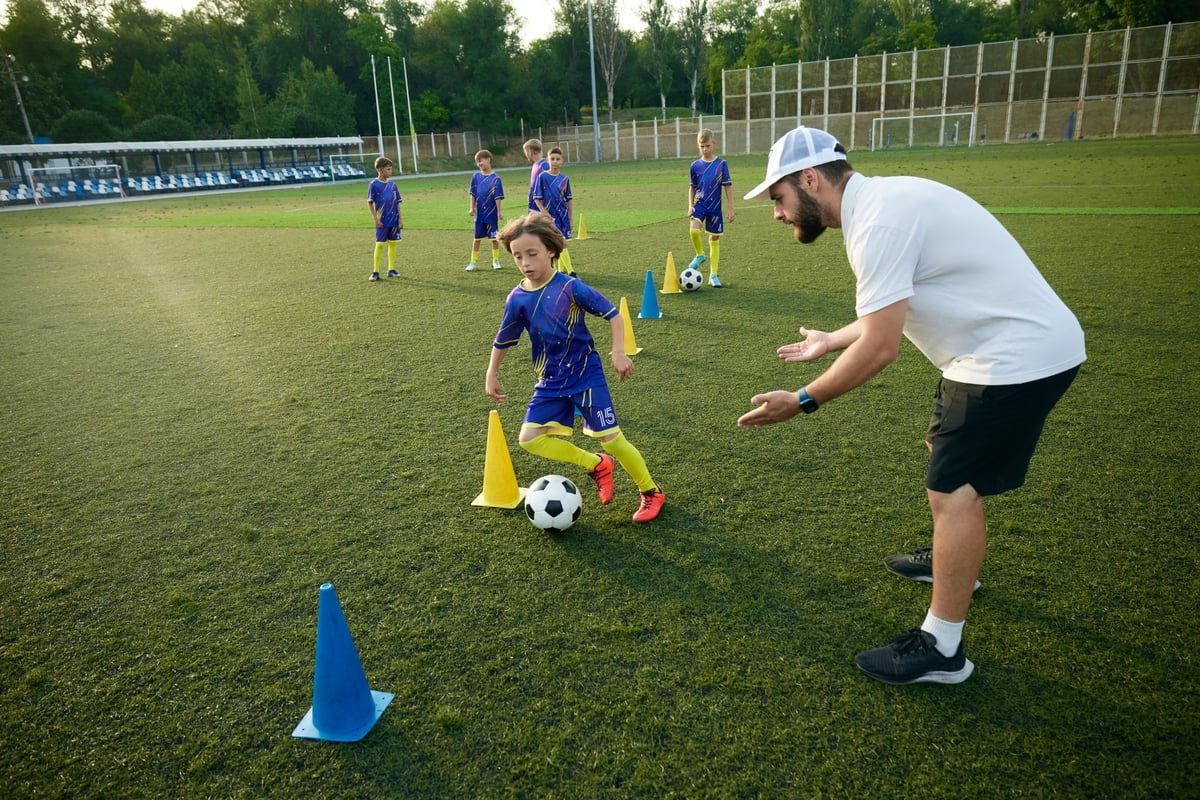 Boy practices dribbling through cones with focused encouragement from the coach
