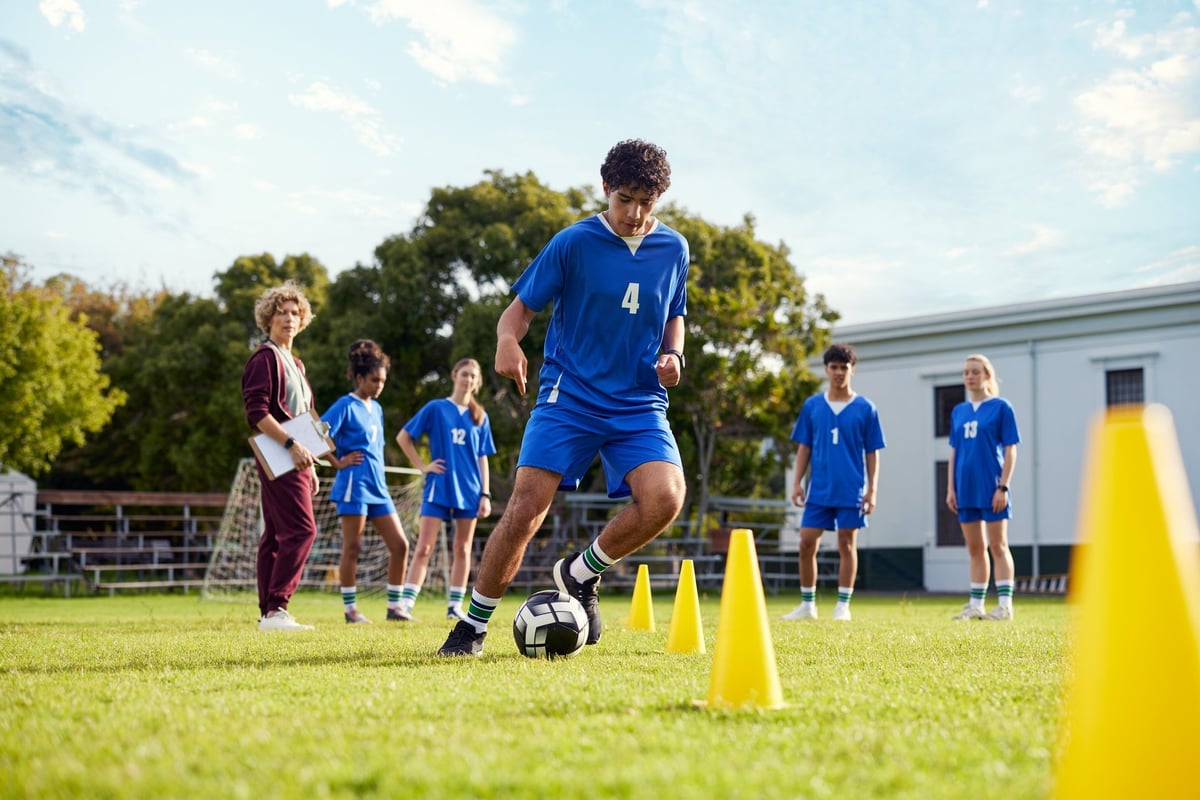 Male teenager player dribbling a soccer ball through yellow cones during training