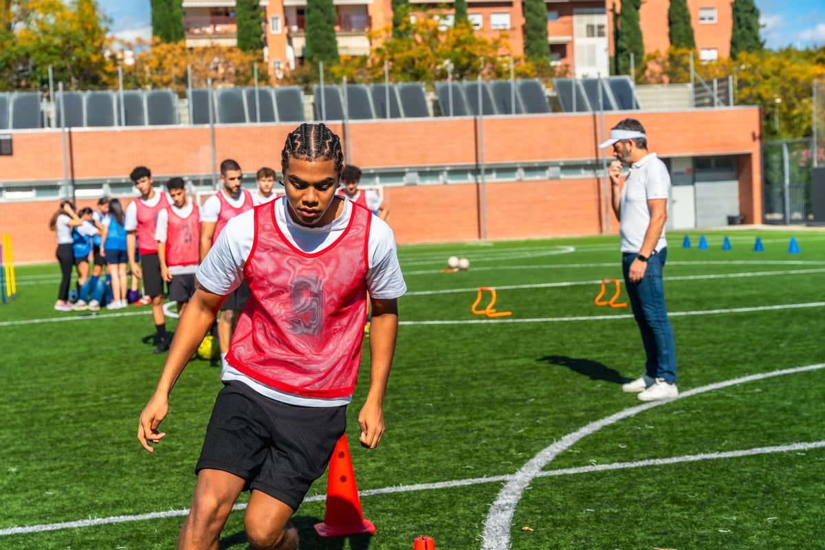 Young male athletes train on green artificial turf practicing soccer drills